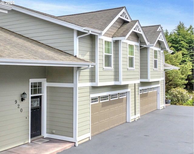 view of home's exterior featuring a garage, roof with shingles, and driveway