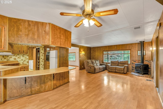 24344 NW Meacham Rd, North Plains, OR 97133 - living area featuring a wood stove, plenty of natural light, light wood-style floors, a ceiling fan, and wood walls