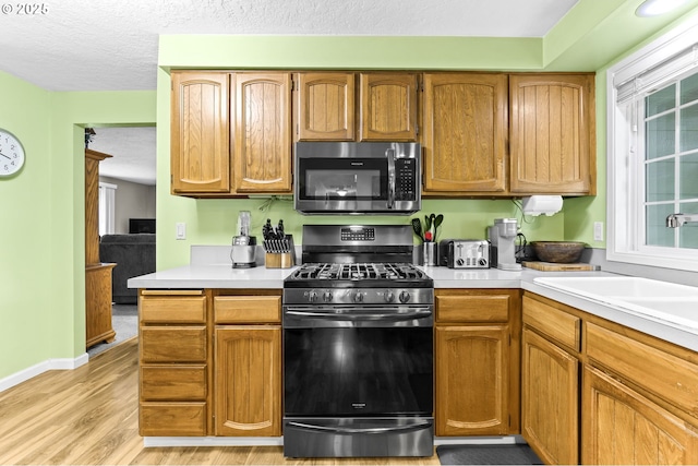 1018 S Holly Ct, Canby, OR 97013 - kitchen featuring stainless steel appliances, light countertops, light wood finished floors, a textured ceiling, and brown cabinets