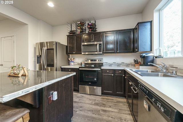 kitchen with stainless steel appliances, sink, light hardwood / wood-style flooring, dark brown cabinets, and a breakfast bar area