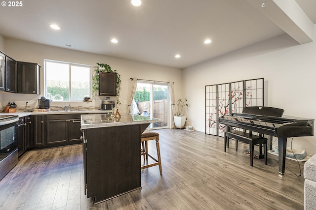 kitchen with a center island, a kitchen bar, light hardwood / wood-style floors, stainless steel range with electric stovetop, and dark brown cabinets