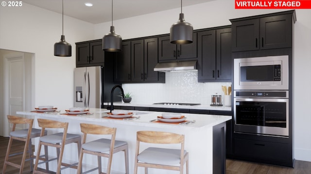 11855 SW Bosley Ter, Beaverton, OR 97007 - kitchen featuring stainless steel appliances, under cabinet range hood, light countertops, a center island with sink, and dark wood finished floors