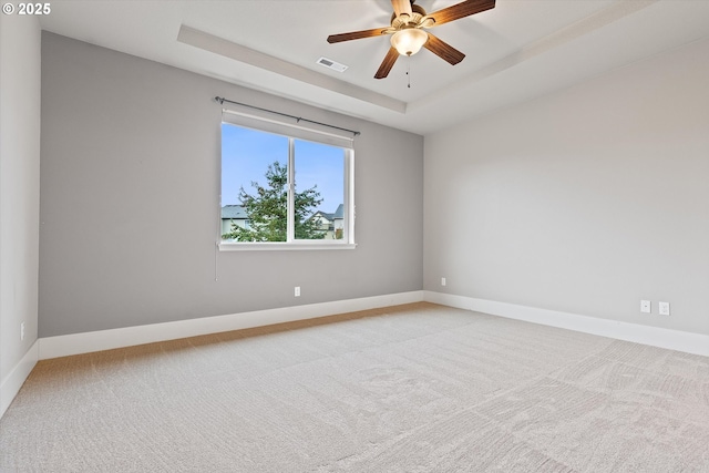 carpeted spare room with a tray ceiling and ceiling fan