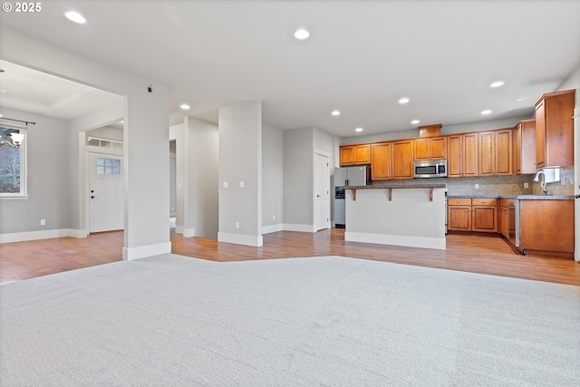 kitchen with a kitchen island, a breakfast bar, tasteful backsplash, stainless steel appliances, and light carpet