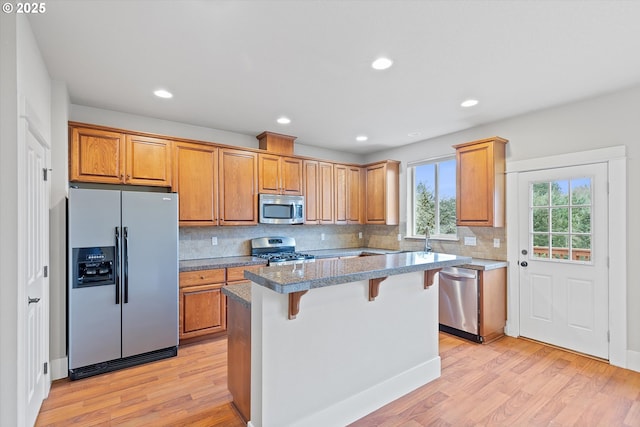 kitchen with a breakfast bar, tasteful backsplash, a center island, light hardwood / wood-style flooring, and appliances with stainless steel finishes