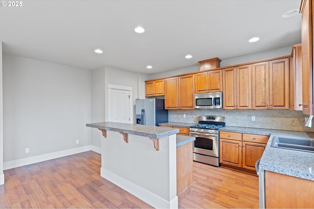 kitchen featuring appliances with stainless steel finishes, a breakfast bar, sink, and light wood-type flooring