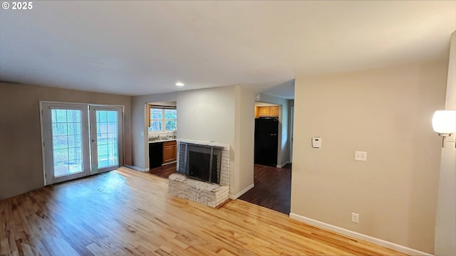 unfurnished living room with french doors, light hardwood / wood-style floors, and a brick fireplace