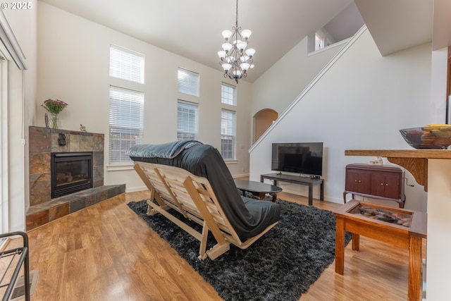 living room featuring a tile fireplace, a high ceiling, wood finished floors, baseboards, and a notable chandelier