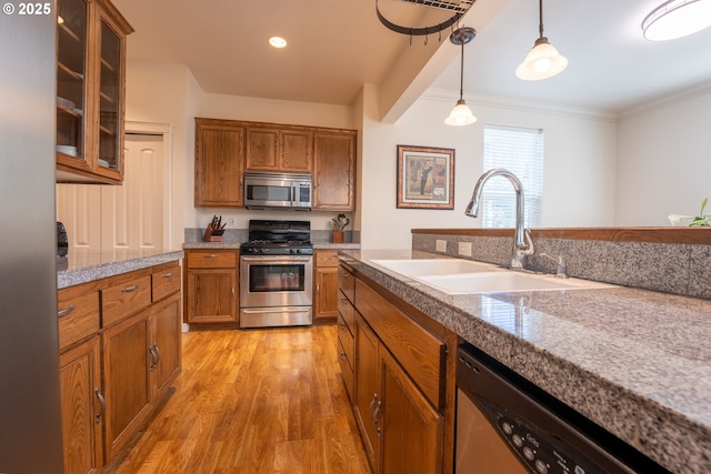 kitchen with a sink, brown cabinets, light wood-style floors, pendant lighting, and appliances with stainless steel finishes
