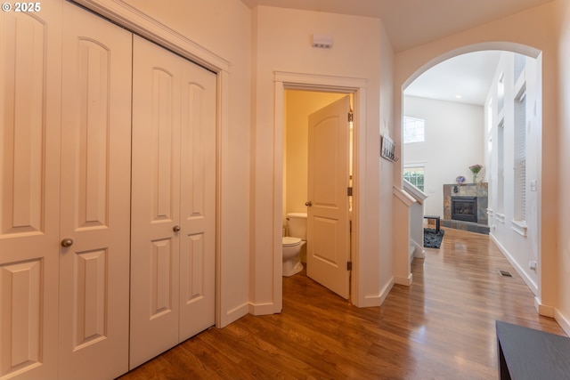 corridor with visible vents, baseboards, arched walkways, and dark wood finished floors