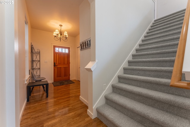 entryway featuring baseboards, wood finished floors, a notable chandelier, and stairway