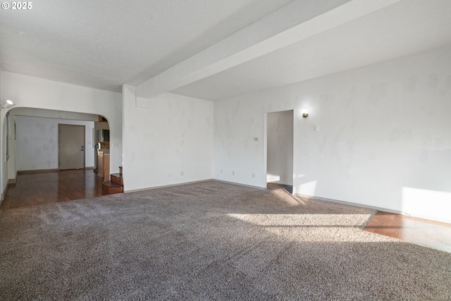 empty room with a textured ceiling, beamed ceiling, and dark colored carpet