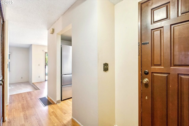 corridor with light wood finished floors, visible vents, a textured ceiling, and baseboards