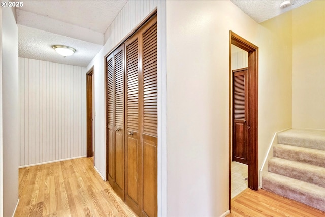 hall featuring stairway, baseboards, a textured ceiling, and light wood finished floors