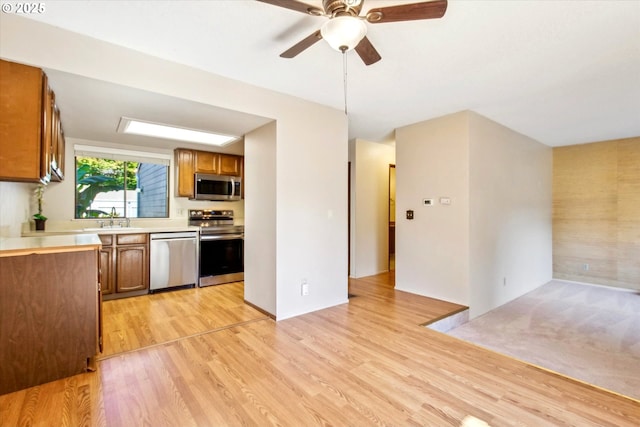 kitchen featuring light countertops, light wood-style flooring, brown cabinetry, stainless steel appliances, and a sink