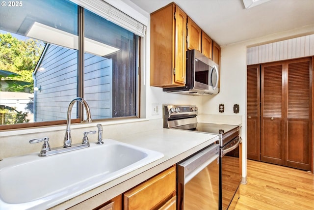 kitchen featuring light countertops, light wood-style flooring, appliances with stainless steel finishes, brown cabinetry, and a sink