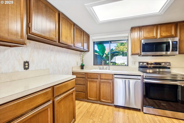 kitchen featuring light wood-type flooring, a sink, light countertops, appliances with stainless steel finishes, and brown cabinets