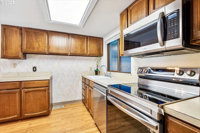 kitchen featuring a sink, stainless steel appliances, light wood finished floors, and light countertops