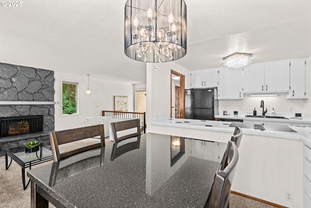 2547 Brittania Pl, Eugene, OR 97405 - kitchen featuring freestanding refrigerator, a textured ceiling, a chandelier, white cabinets, and a stone fireplace