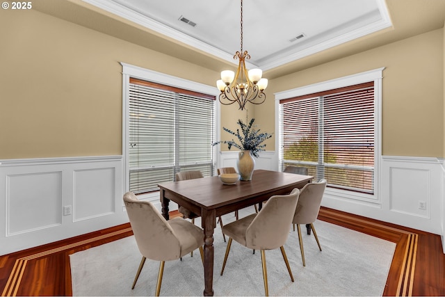 dining area with a chandelier, a raised ceiling, visible vents, and a wainscoted wall