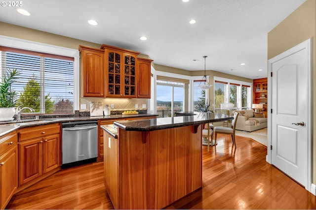 kitchen with dishwasher, glass insert cabinets, a breakfast bar, a center island, and a sink