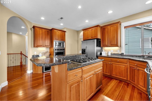 kitchen featuring a kitchen island, appliances with stainless steel finishes, dark stone countertops, light wood-style floors, and a sink