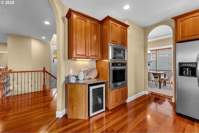 kitchen with stainless steel appliances, wine cooler, backsplash, and arched walkways