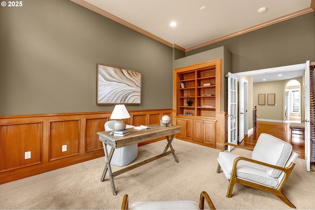 office area with built in shelves, arched walkways, light colored carpet, and ornamental molding