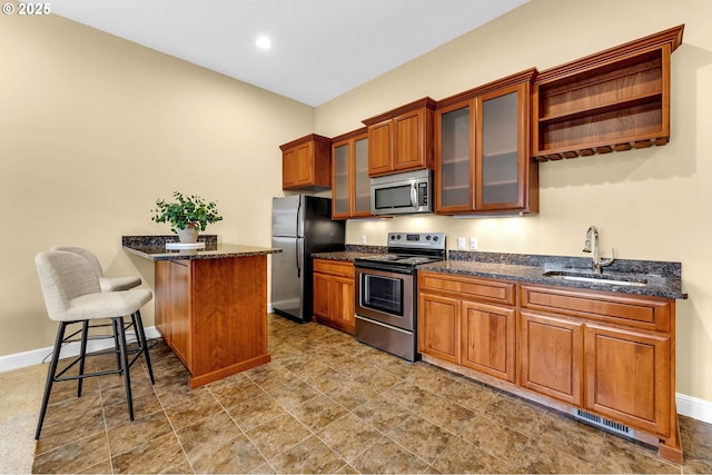 kitchen with a breakfast bar, stainless steel appliances, brown cabinetry, a sink, and a peninsula