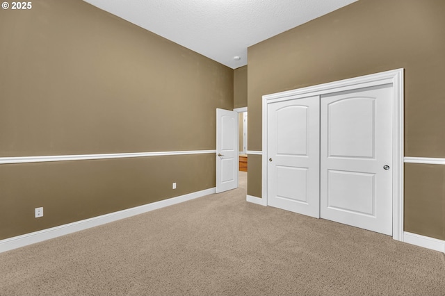 unfurnished bedroom featuring baseboards, a closet, a textured ceiling, and light colored carpet