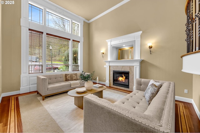 living area featuring a fireplace, a high ceiling, ornamental molding, wood finished floors, and baseboards