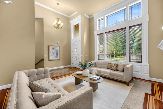 living room featuring a high ceiling, an inviting chandelier, ornamental molding, wood finished floors, and baseboards