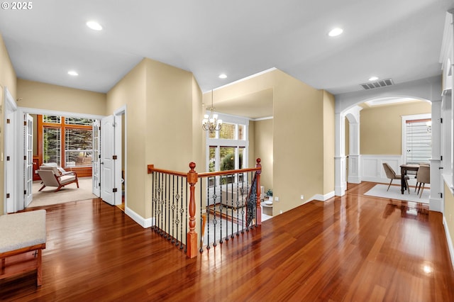 hallway with arched walkways, wood finished floors, an upstairs landing, and visible vents