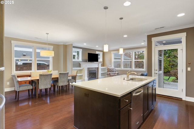 kitchen with dark brown cabinets, pendant lighting, sink, a kitchen island with sink, and ornamental molding