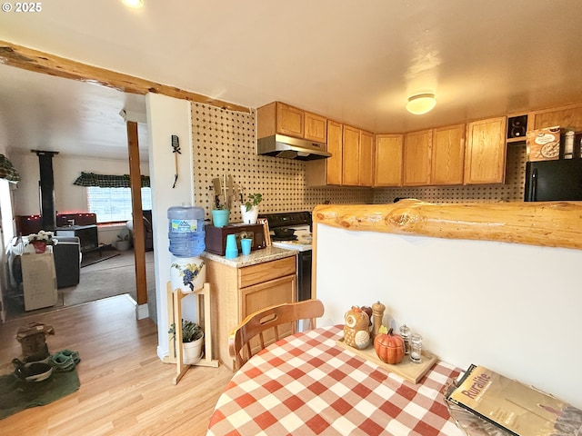 kitchen with light countertops, freestanding refrigerator, a wood stove, range with electric cooktop, and under cabinet range hood