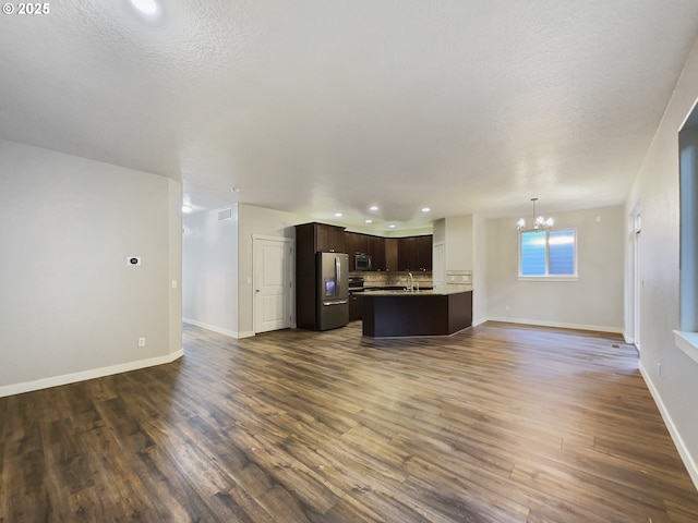 unfurnished living room with a textured ceiling, an inviting chandelier, dark wood-type flooring, and sink