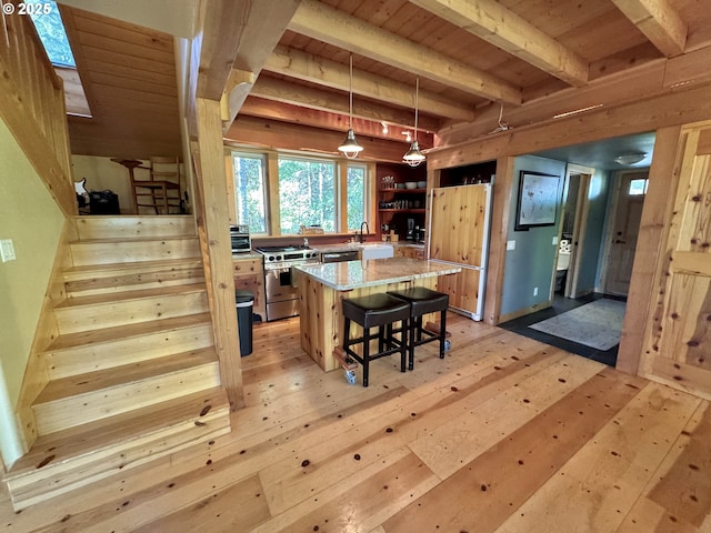 kitchen with appliances with stainless steel finishes, decorative light fixtures, a breakfast bar area, a center island, and light stone counters