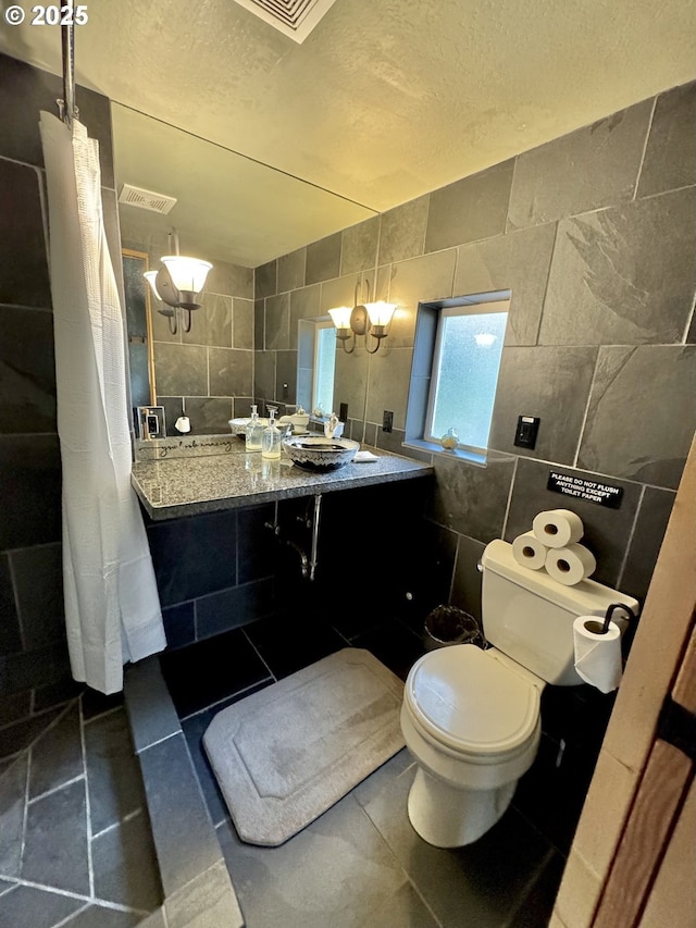 bathroom featuring tile walls, tile patterned floors, toilet, and a textured ceiling