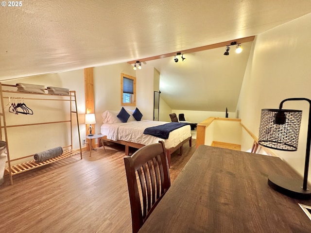 bedroom with rail lighting, vaulted ceiling, hardwood / wood-style floors, and a textured ceiling