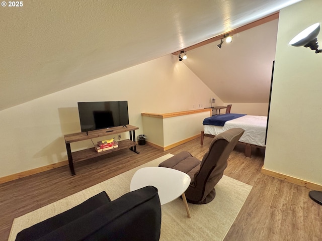 bedroom with vaulted ceiling, rail lighting, a textured ceiling, and light wood-type flooring