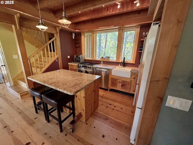 kitchen featuring pendant lighting, sink, appliances with stainless steel finishes, light hardwood / wood-style floors, and a kitchen island