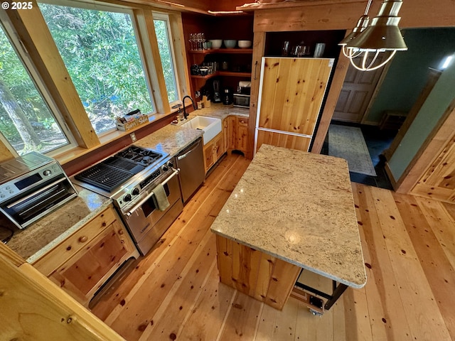 kitchen featuring sink, light hardwood / wood-style flooring, stainless steel appliances, light stone countertops, and decorative light fixtures