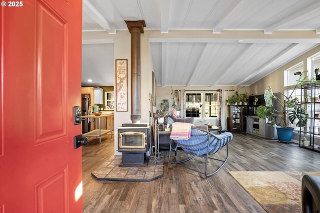 living room featuring wood-type flooring, a wealth of natural light, lofted ceiling with beams, and a wood stove