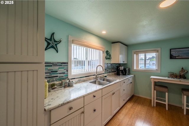 kitchen with a sink, light wood finished floors, tasteful backsplash, white cabinetry, and baseboards