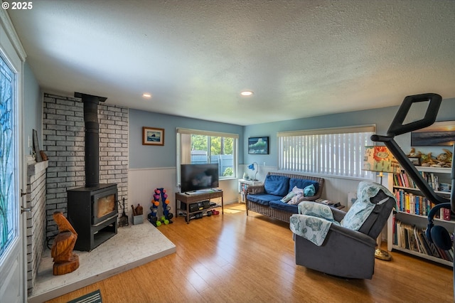 living room featuring a wood stove, a wainscoted wall, a textured ceiling, wood finished floors, and recessed lighting