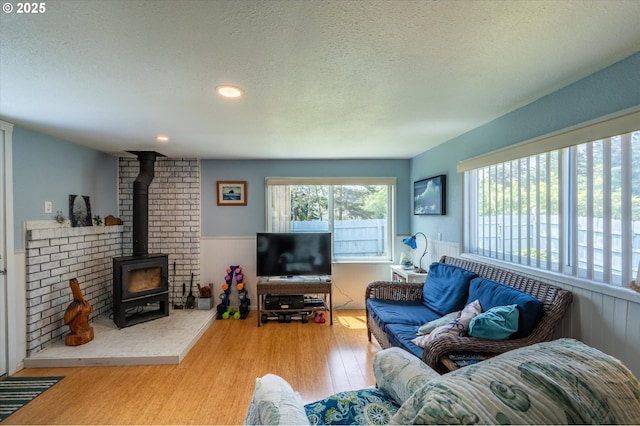 living area featuring a textured ceiling, wood finished floors, wainscoting, and a wood stove