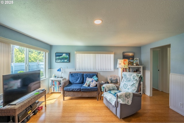 living area featuring a textured ceiling, a wainscoted wall, and wood finished floors