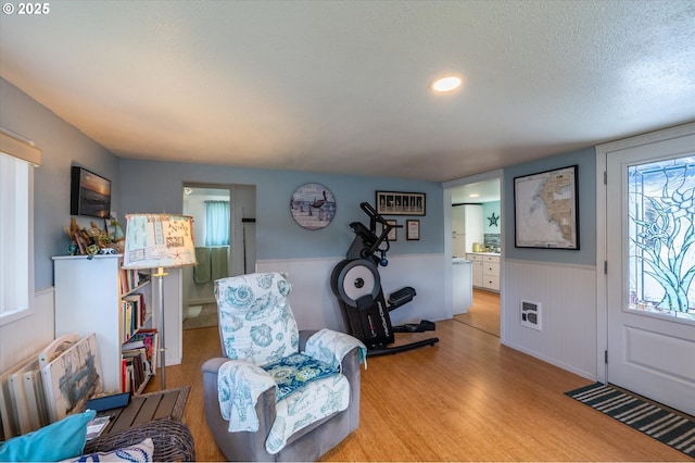 living room featuring wainscoting, light wood-style flooring, and a textured ceiling