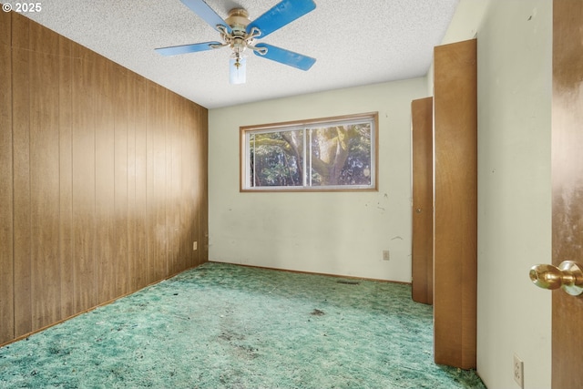 empty room featuring ceiling fan, wooden walls, a textured ceiling, and carpet flooring