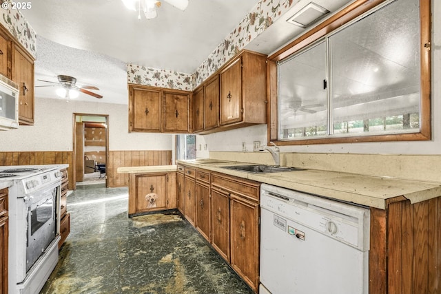 kitchen featuring sink, wood walls, white appliances, a textured ceiling, and ceiling fan